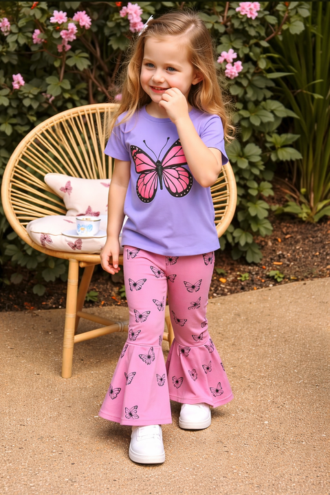 Young girl wearing a purple shirt with a butterfly design and pink pants with butterfly patterns, standing outdoors.