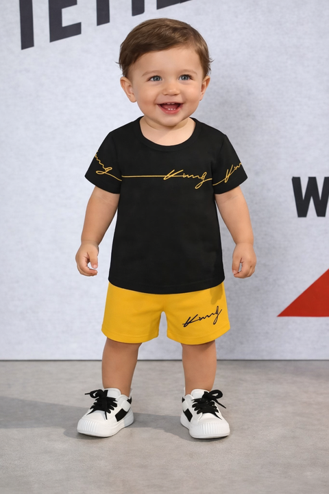 Child wearing a black t-shirt with yellow text and yellow shorts, standing against a gray background.