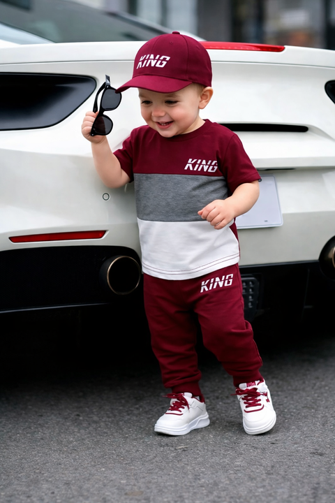 Child wearing a maroon and gray 'KING' outfit standing next to a white car.
