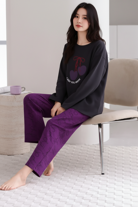 Person wearing a black sweater with a cherry design and purple pants sitting on a chair.