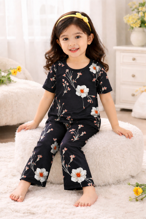Child wearing a black floral pajama set sitting on a white cushion.