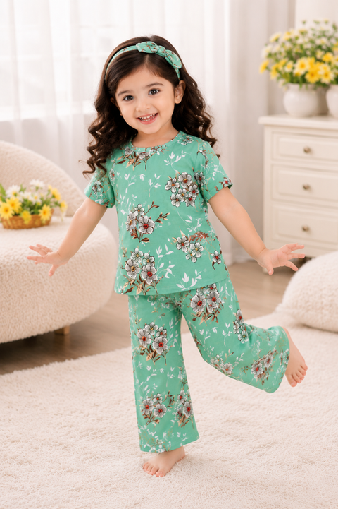Child wearing a green floral pajama set in a room with white curtains and a white dresser.