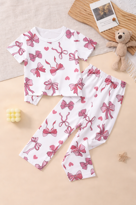 Children's pajama set with pink bow and heart patterns on a beige surface.