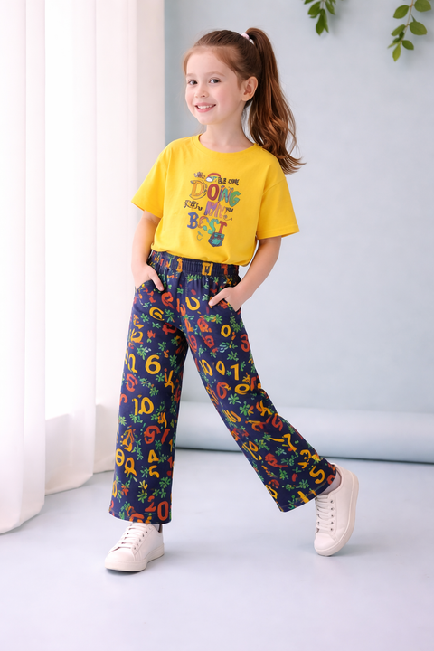 Child wearing a yellow shirt and colorful pants with numbers and letters, standing indoors.