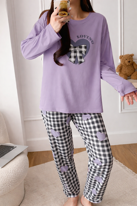 Person wearing a purple long-sleeve top with a heart design and checkered pants, holding a phone.