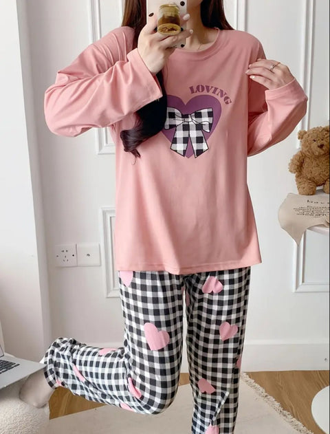 Person wearing pink pajama top with heart design and checkered pants with heart shapes, standing in a room.
