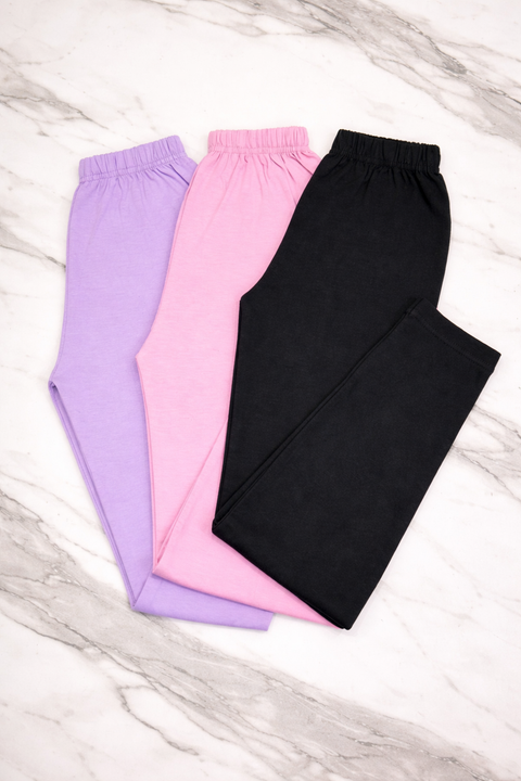 Three pairs of pants in black, pink, and purple on a marble surface