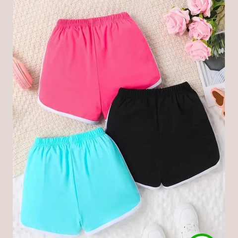 Three pairs of colorful shorts (pink, black, and blue) on a textured surface with flowers in the background.