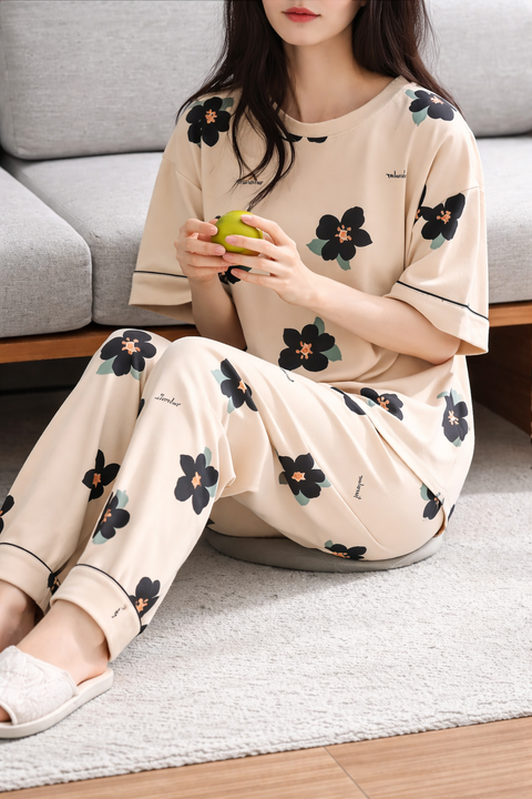 Woman in floral pajama set sitting on a rug holding an apple.