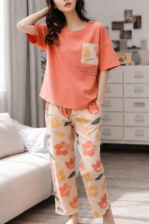 Woman wearing a coral t-shirt and floral pants in a room with a bed and dresser.