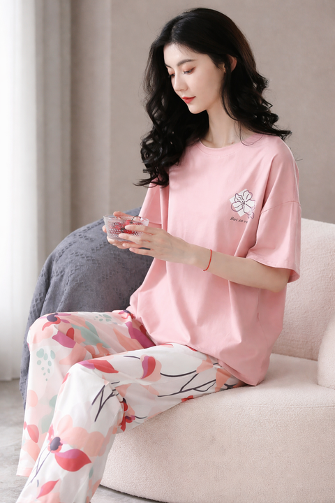 Woman wearing a pink top and floral pants sitting on a couch.