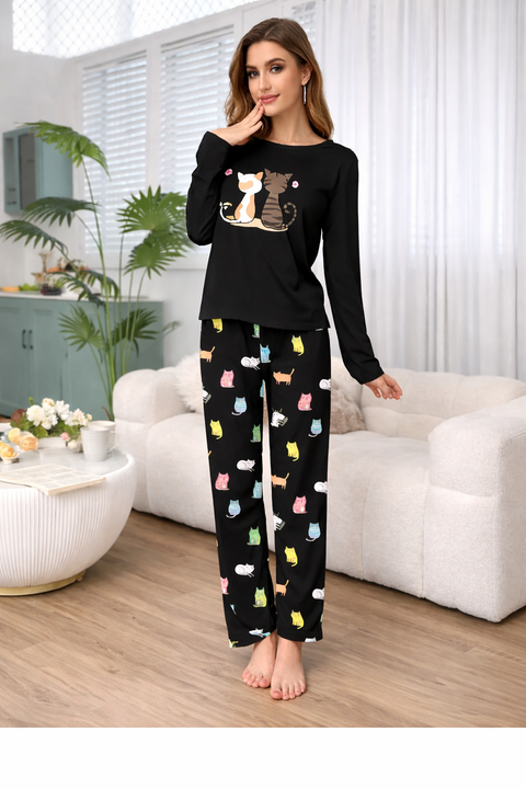 Woman wearing black pajama set with cat designs in a living room.
