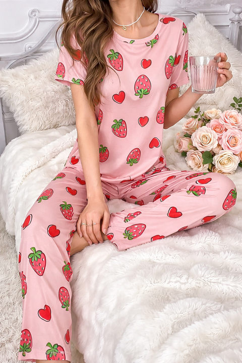 Woman wearing pink pajamas with strawberry pattern, sitting on a white bed holding a glass.