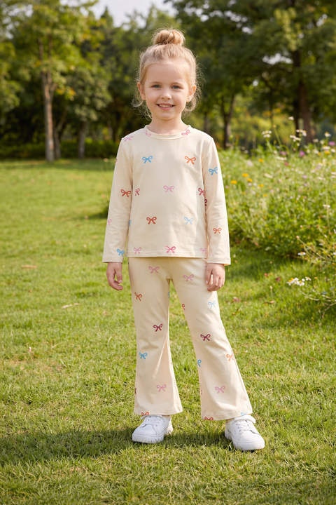 Young girl in a beige outfit with butterfly patterns standing in a grassy field.