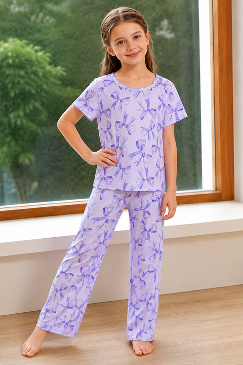 Young girl wearing purple pajamas with a butterfly pattern in a room with a window.